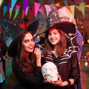 Beautiful young witch holding a human skull and smiling to the camera at halloween party. Witches looking into the camera.