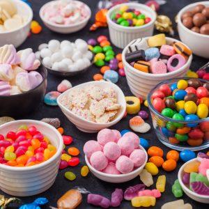 Pink lollipop candies in jar with various milk chocolate and jelly gums candies on black with liquorice allsorts and strawberry bonbons and large variety of sweets and candies.